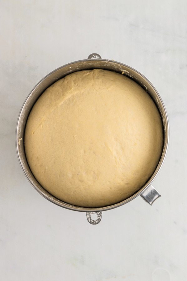 Risen dough in a metal mixing bowl.