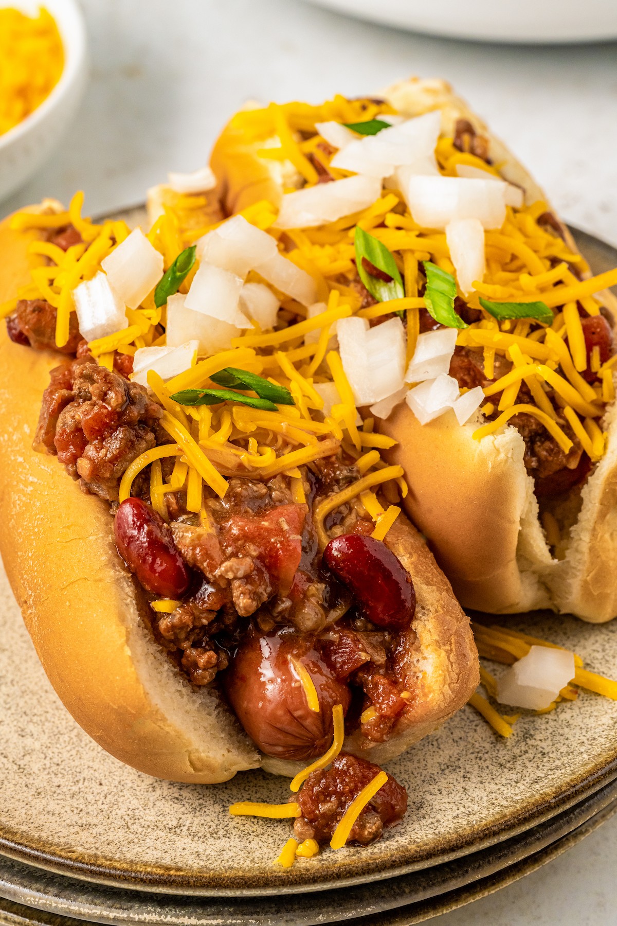 Two hot dogs topped with chili, cheese, and chopped onion.