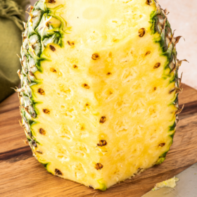 A pineapple on a cutting board being cut with a knife.