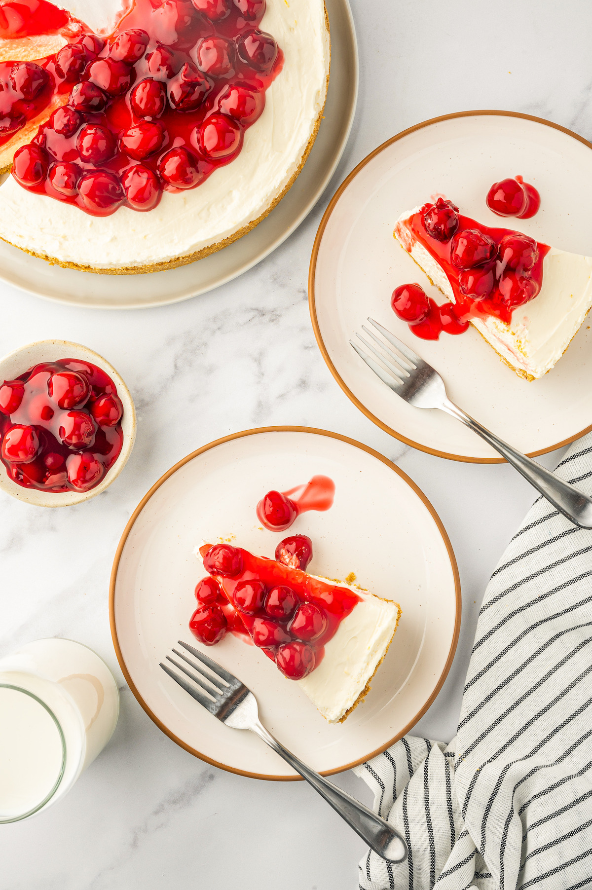 Overhead shot of two slices of cheesecake on dessert plates next to the whole cheesecake.