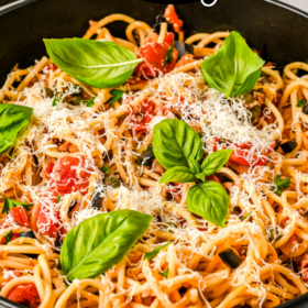 Spaghetti Puttanesca in a large skillet topped with fresh basil and grated Parmesan cheese.