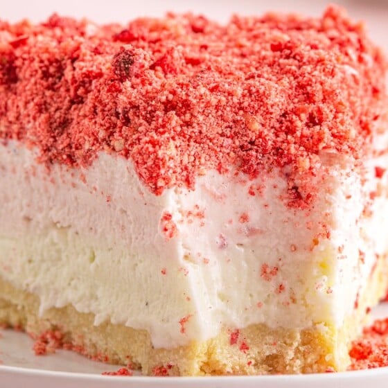 A slice of strawberry shortcake ice cream on a plate with a bite taken out of it.