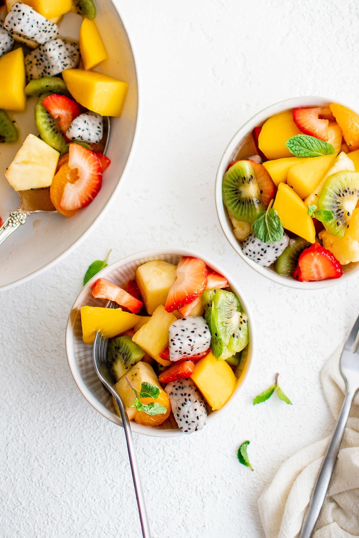 Two servings of fruit salad next to a large bowl.