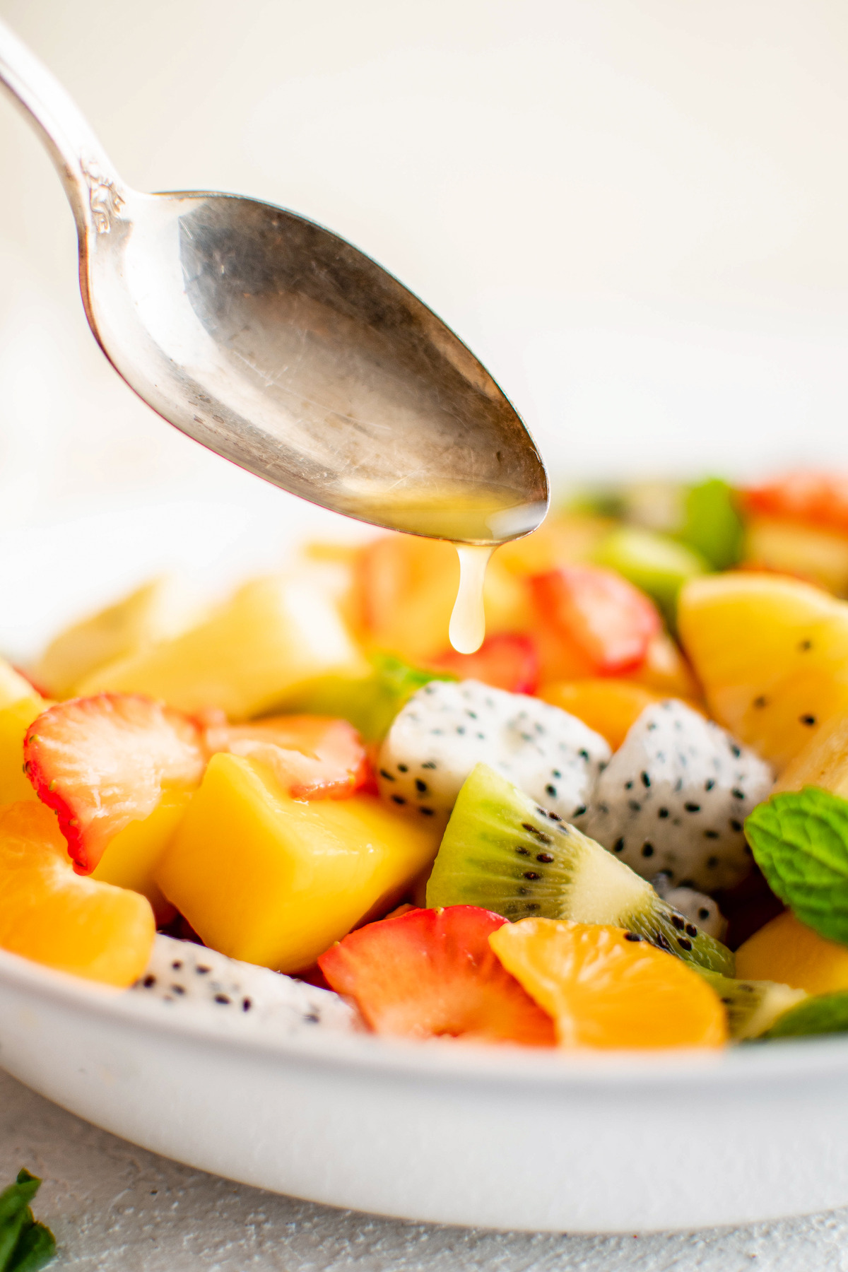 Spooning dressing over a bowl of mixed fresh fruit.
