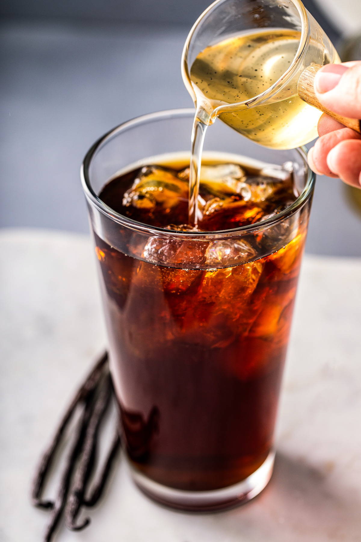 Pouring syrup into a glass of iced coffee.