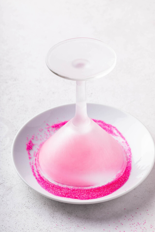 Chilled martini glass being rimmed with pink sugar.