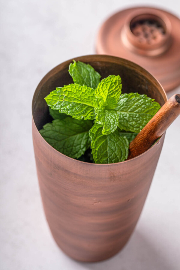 Mint in a cocktail shaker with a wooden spoon.