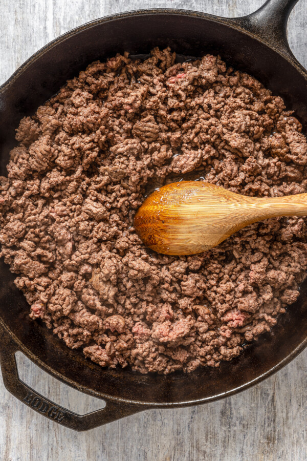 Ground beef in a cast iron skillet with a wooden spoon.