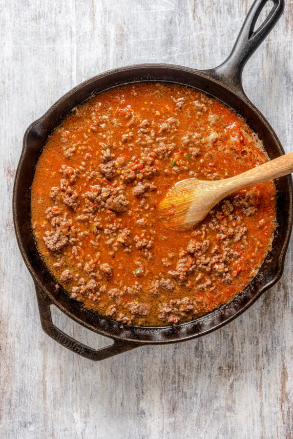 Sauce simmering with ground beef with a wooden spoon.