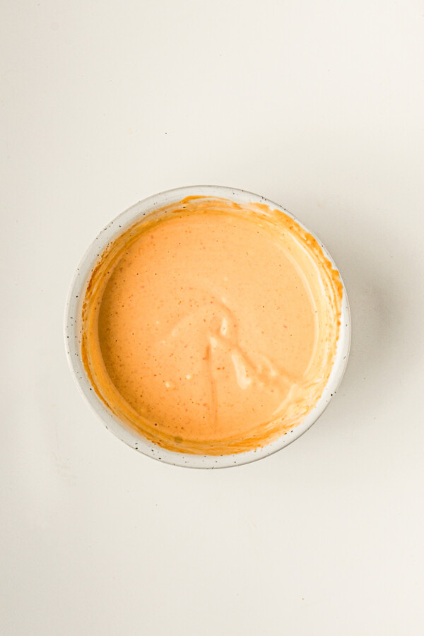 Overhead shot of pale orange, creamy sauce in a white bowl.