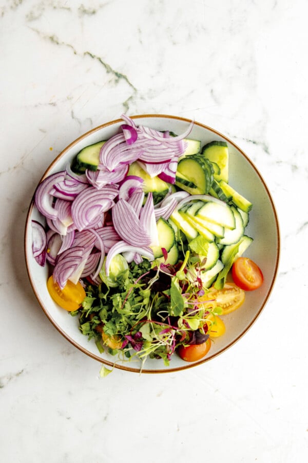 Red onion, cucumbers, and other ingredients in a salad bowl.