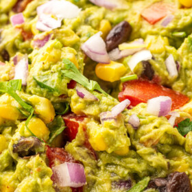 A bowl of loaded guacamole with cilantro on top.