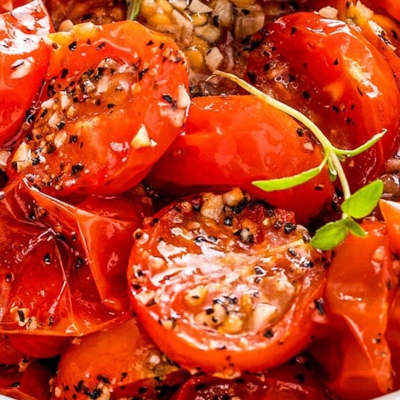 Garlic roasted cherry tomatoes in a bowl with fresh herbs on top.