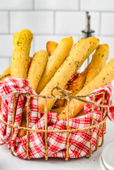 Breadsticks gathered into a wire basket lined with a red-checkered cloth.