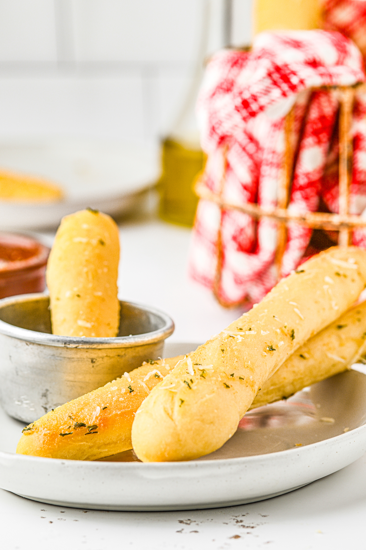 Two homemade breadsticks on a plate, with one dunked in a metal cup of dipping sauce.