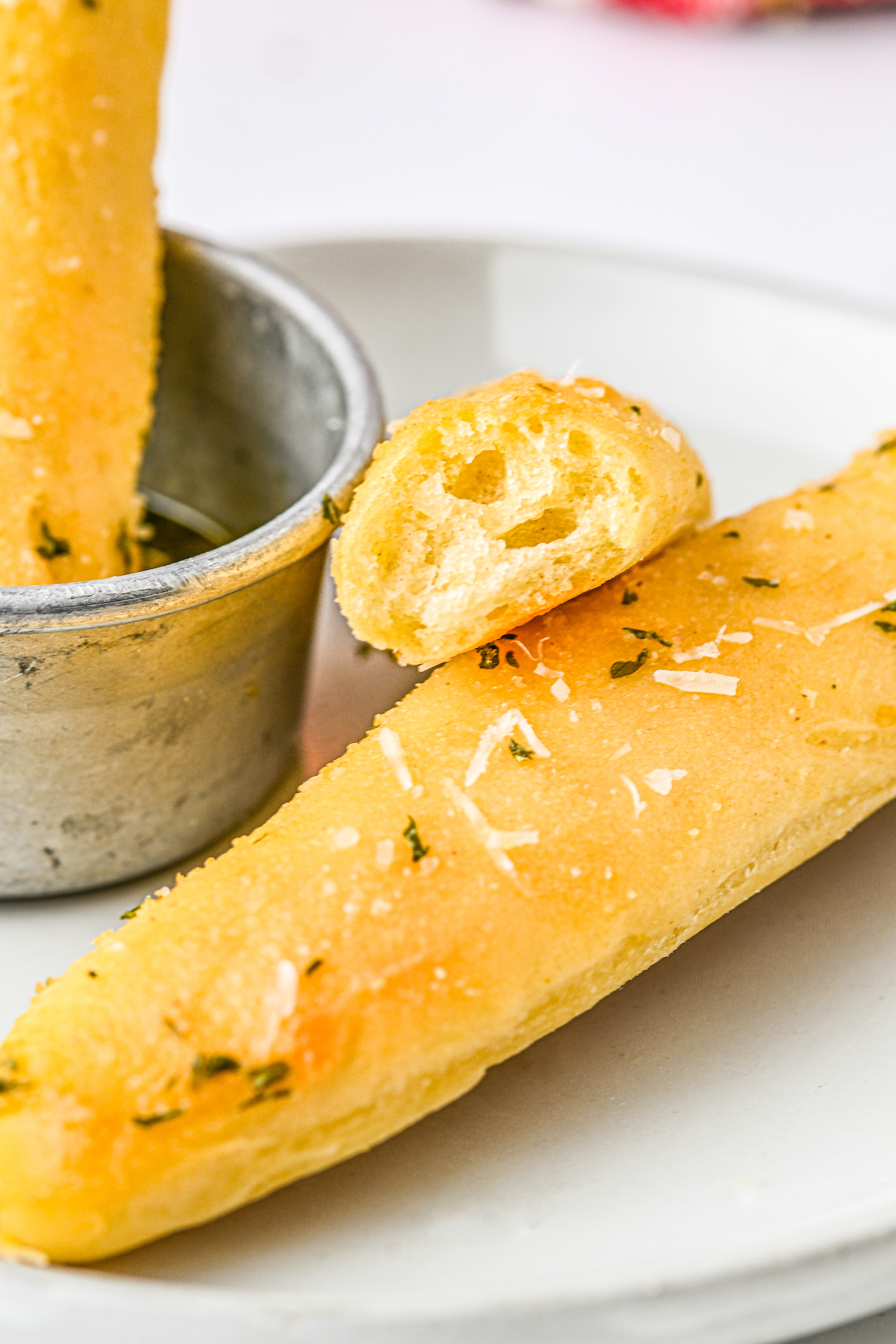 Breadsticks on a plate. One has been broken in half and turned toward the camera, to show the texture.