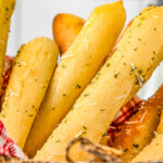 Landscape shot of homemade bread sticks in a basket lined with a red-checked cloth napkin.