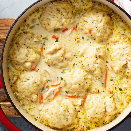 Homemade Chicken and Dumplings with big homemade dumplings in a pot on a wooden cutting board.