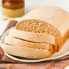 A partially-sliced loaf of honey wheat bread on a plate.