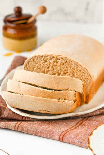 A partially-sliced loaf of honey wheat bread on a plate.