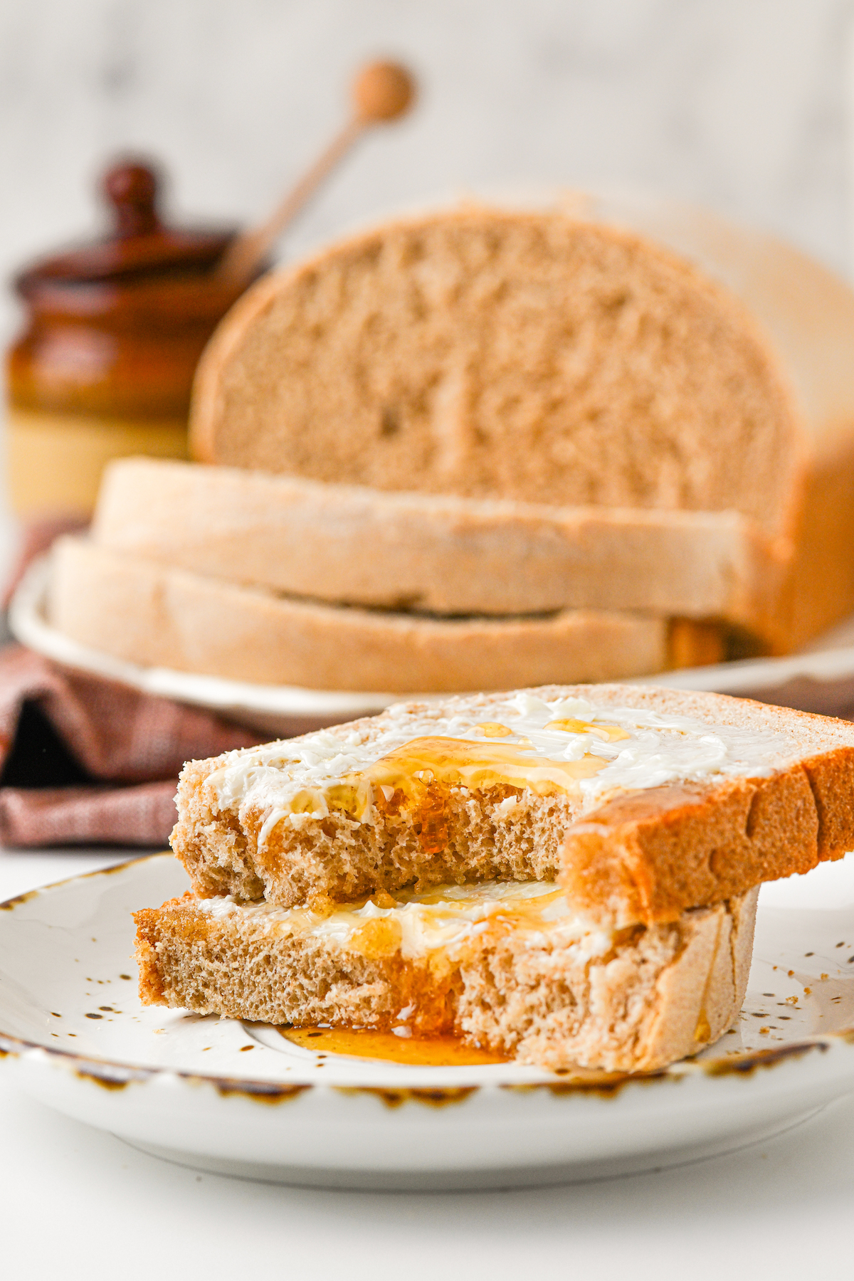 A slice of buttered bread with honey, broken in half, with a bite taken out of one of the halves.