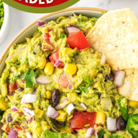 Loaded guacamole dip in a bowl with tortilla chips on the side.