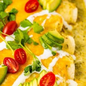 Sausage breakfast enchiladas in a baking dish topped with avocado, cilantro and more.