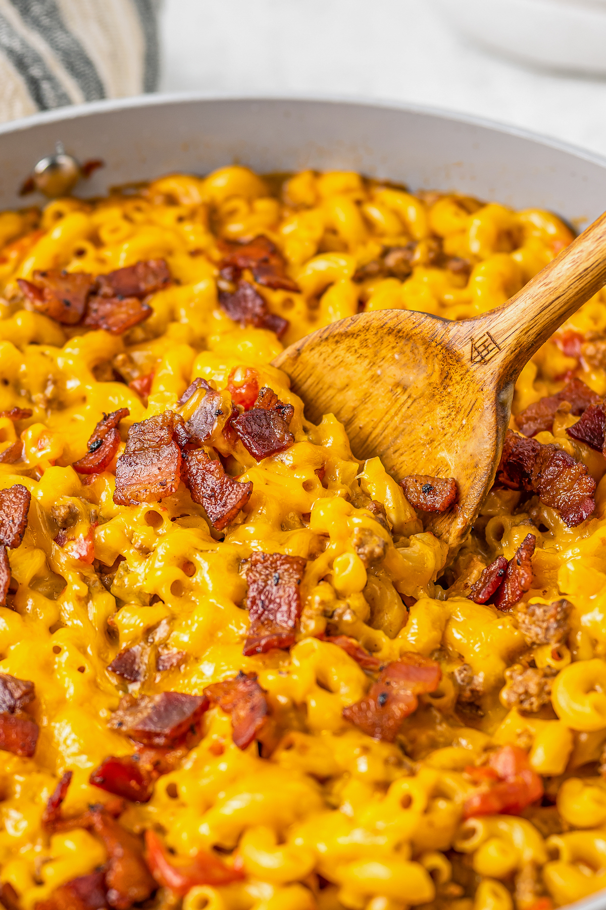 A wooden spoon resting in a skillet of cheeseburger macaroni.