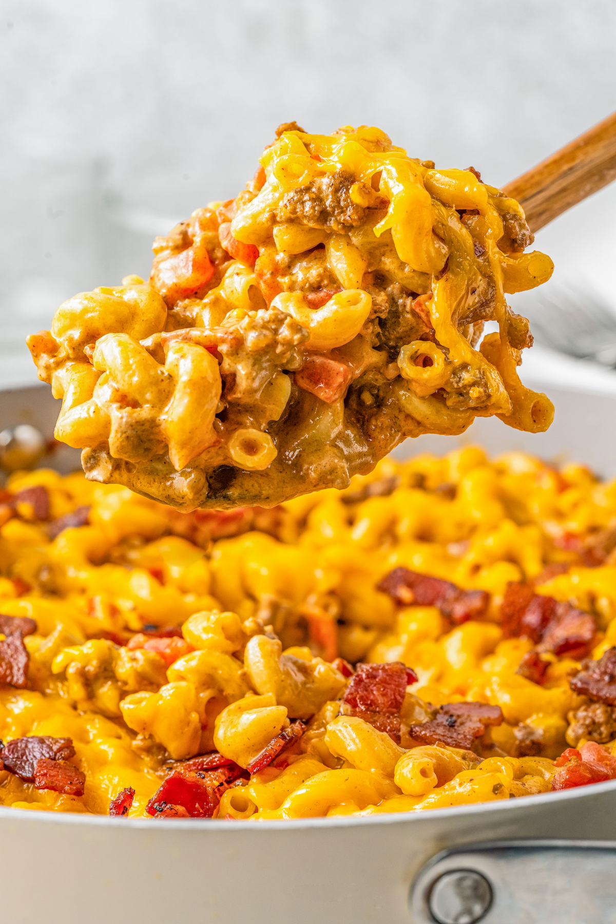 Lifting a scoop of cheeseburger mac and cheese out of a skillet.