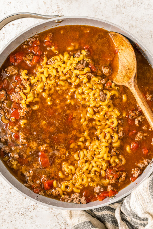 Adding broth and pasta to a skillet.