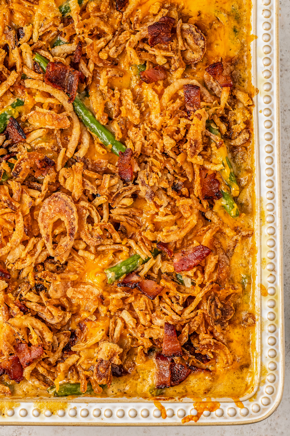 Close-up shot of a green bean casserole with cheese, bacon and crispy fried onions on top in a glass baking dish.