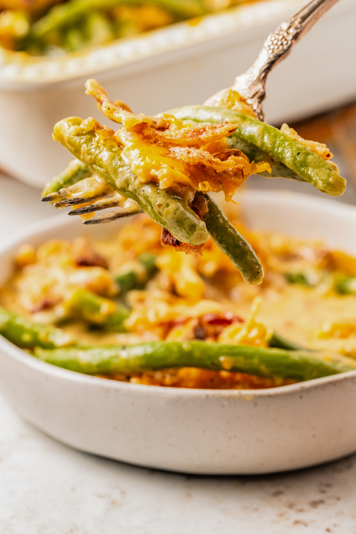 Lifting a forkful of cheesy green bean casserole toward the camera.