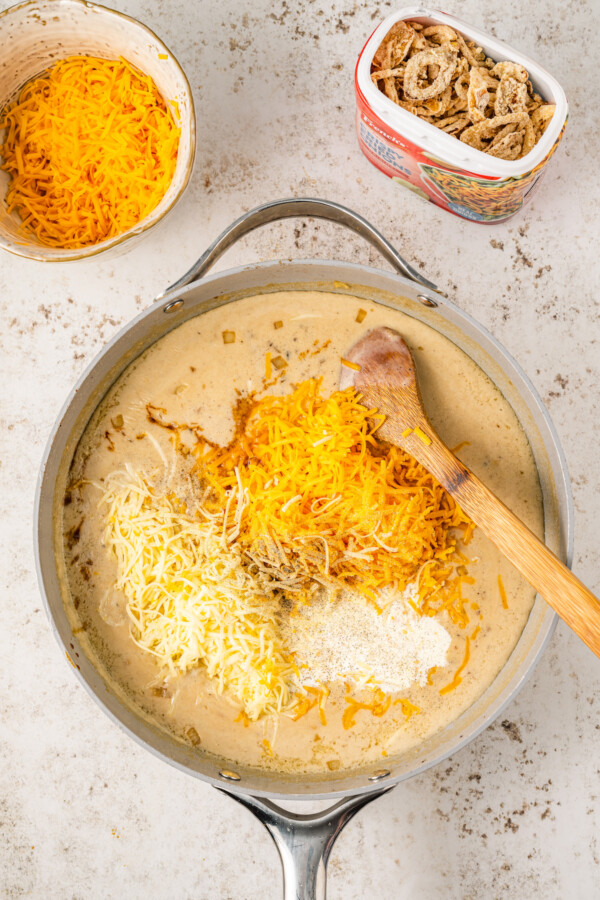 Adding shredded cheese to a homemade cream sauce.