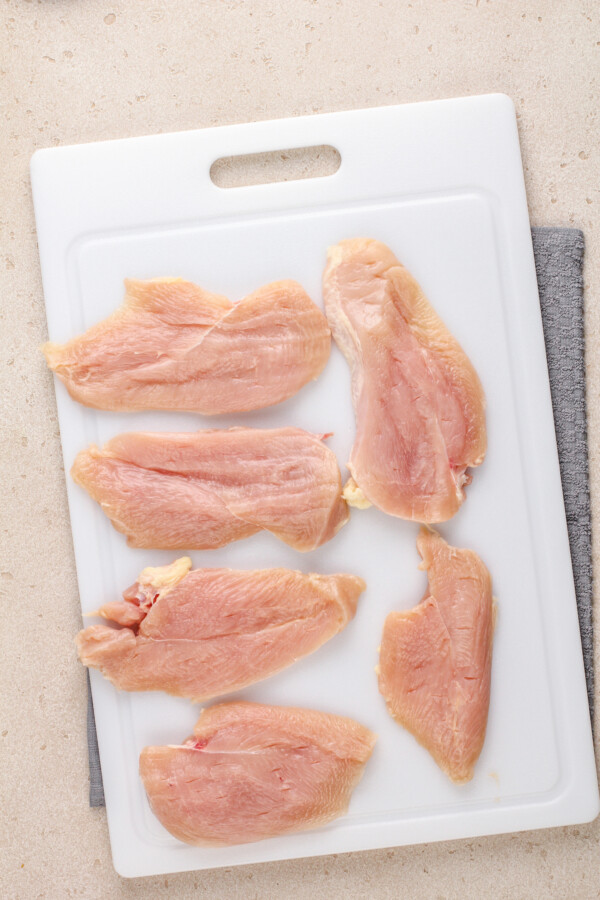 Raw chicken breasts cut into then cutlets on a cutting board.