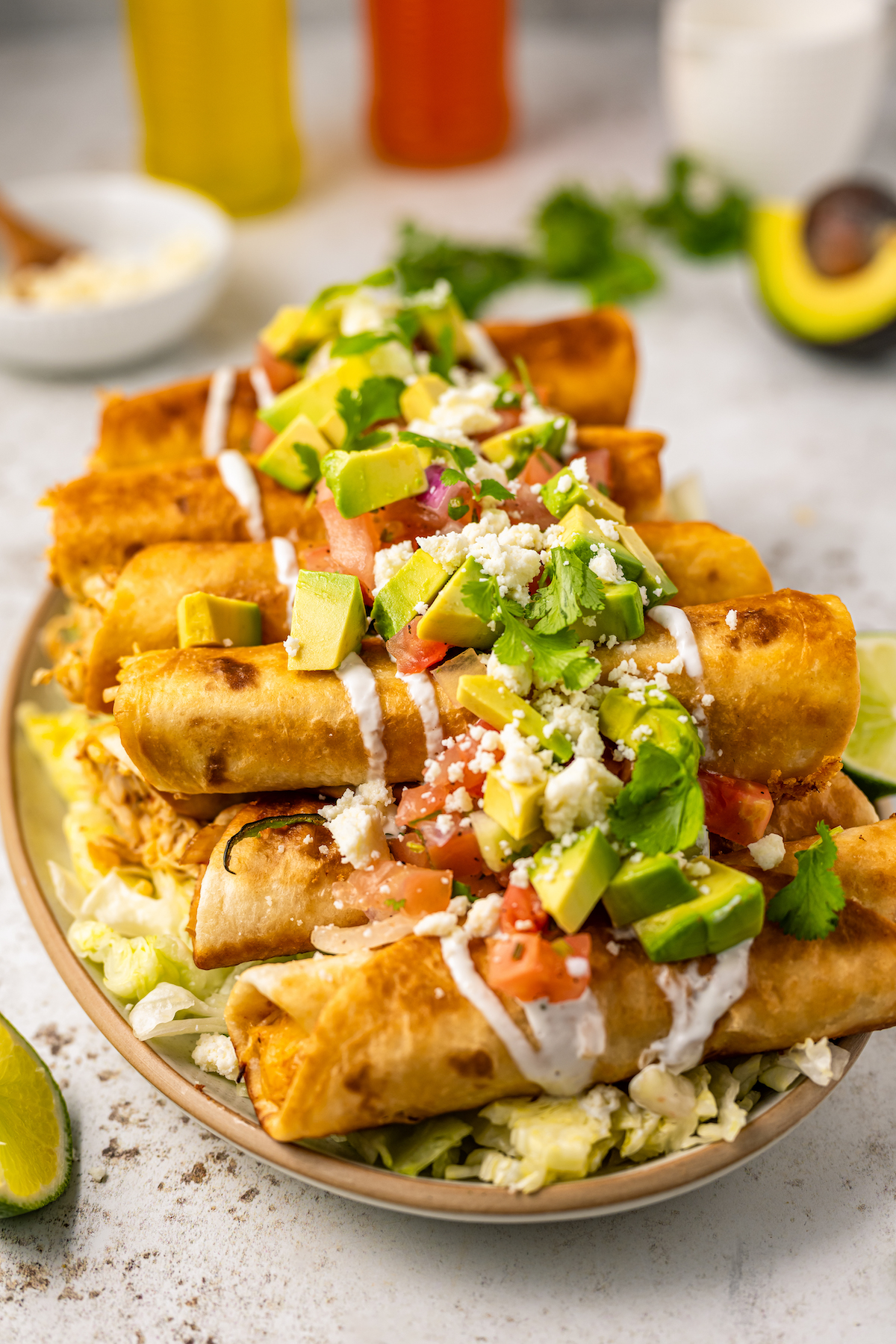 Taquitos stacked on a platter with all the toppings piled on top.