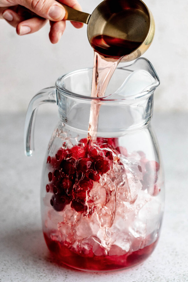 Pouring juice into the pitcher of ice and cranberries.