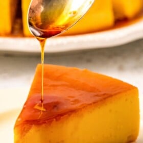 A spoon drizzling caramel sauce over a slice of flan.