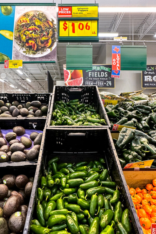 Jalapeños piled into a container at the grocery store with other vegetables.