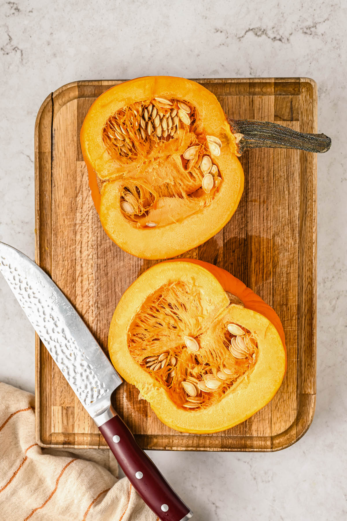 Pumpkin halves on a cutting board with a knife.