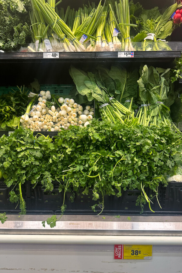 Shelves of refrigerated vegetables and herbs at the grocery store.