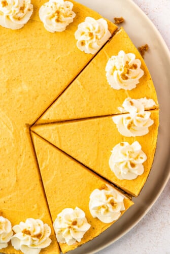 Overhead shot of a partially-sliced cheesecake decorated with piped whipped cream and cookie crumbs.