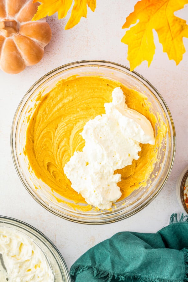 Whipped cream added to a bowl of cheesecake batter.