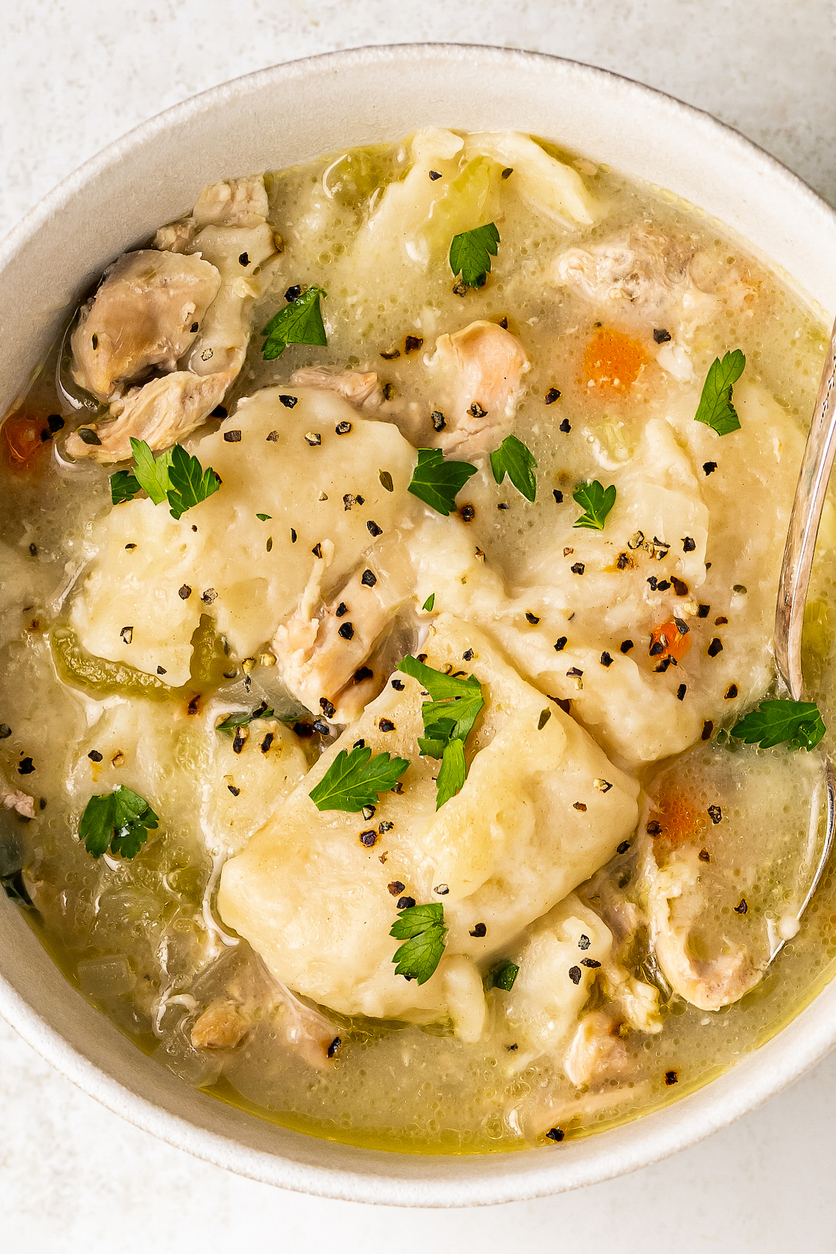 Close-up, overhead shot of a bowl of southern chicken and dumplings garnished with parsley and freshly cracked black pepper.