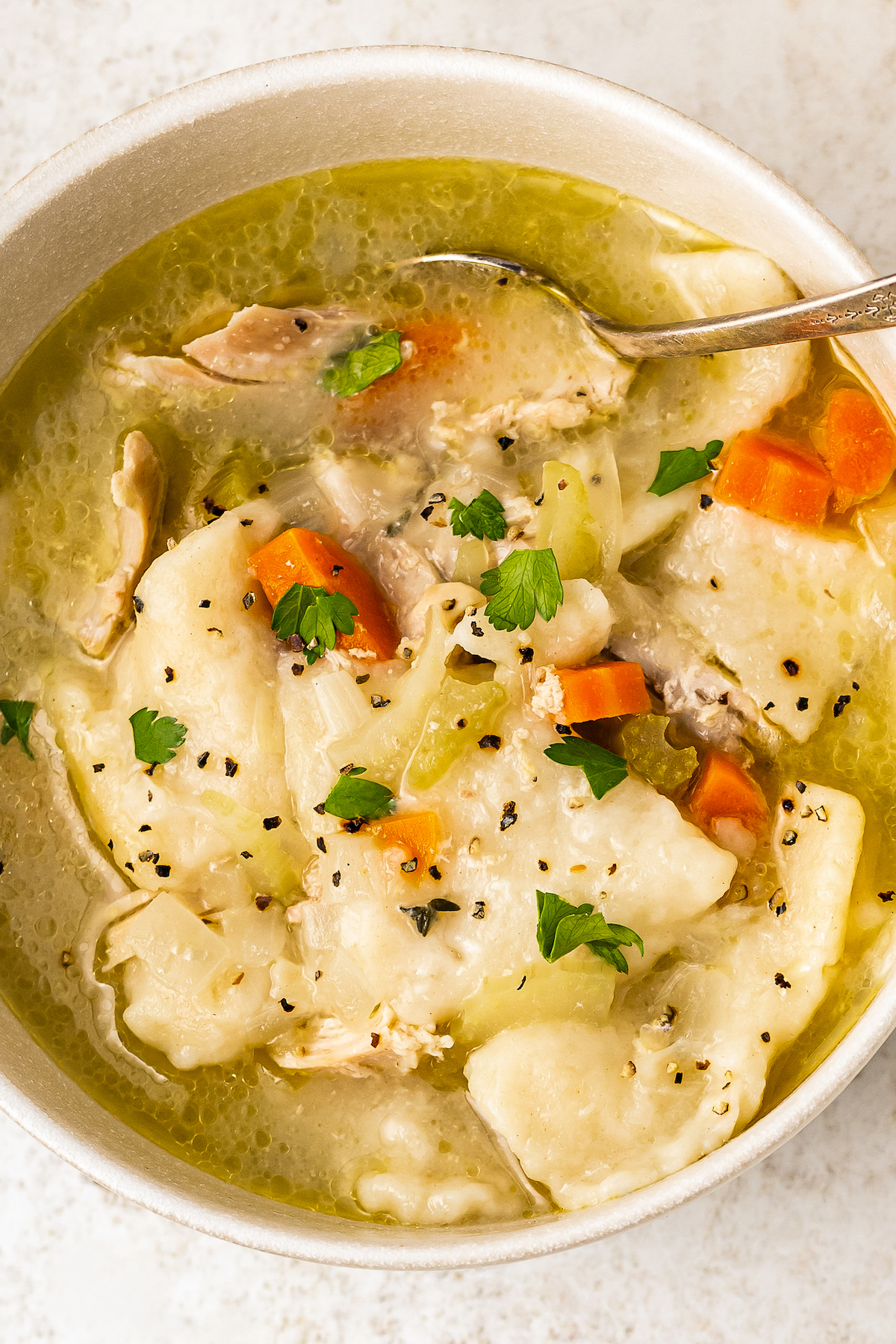 A spoon resting in a bowl of chicken soup with dumplings.