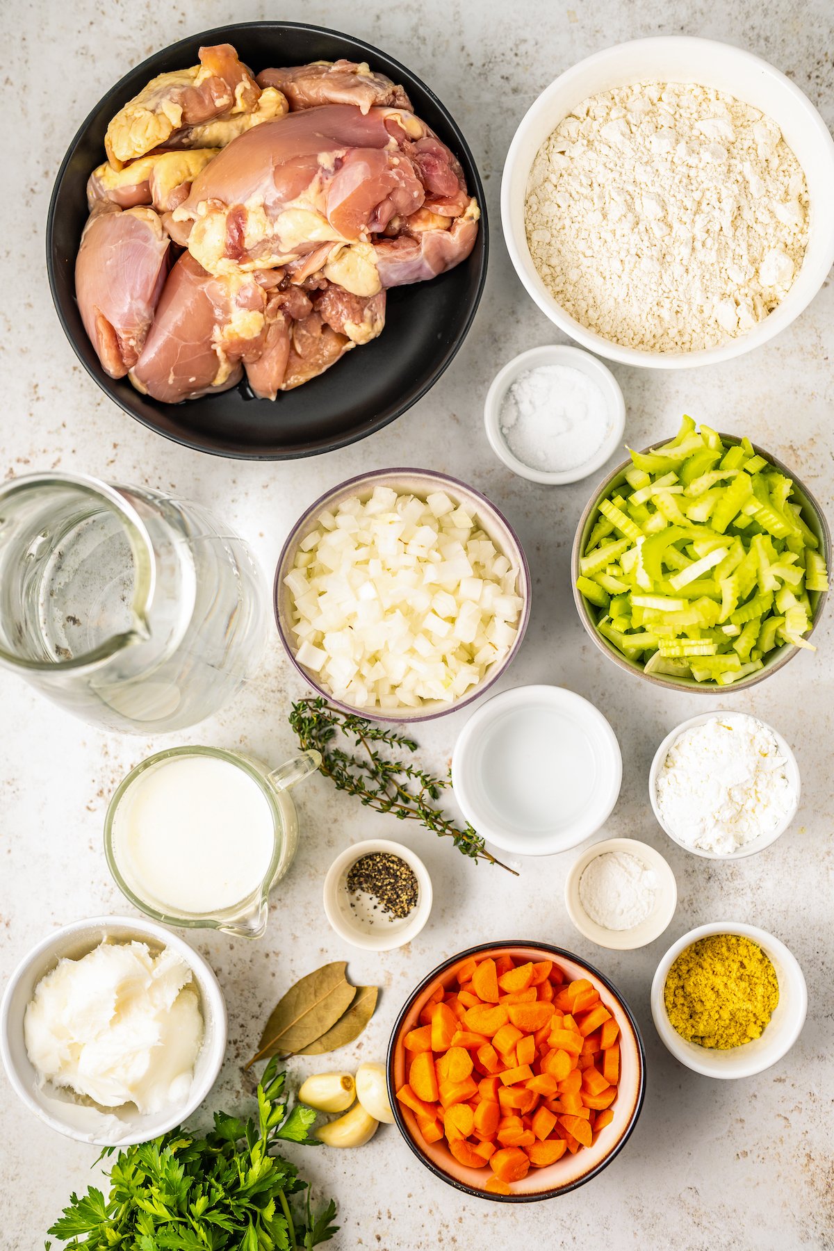 Ingredients for old fashioned chicken and dumplings recipe, arranged in bowls on a work surface.