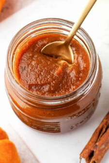 Overhead shot of pumpkin butter in a glass jar with a spoon.