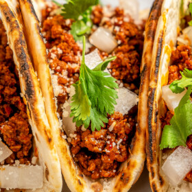 Spicy taco meat wrapped in tortillas with onion, cilantro and crumbled cheese on top.