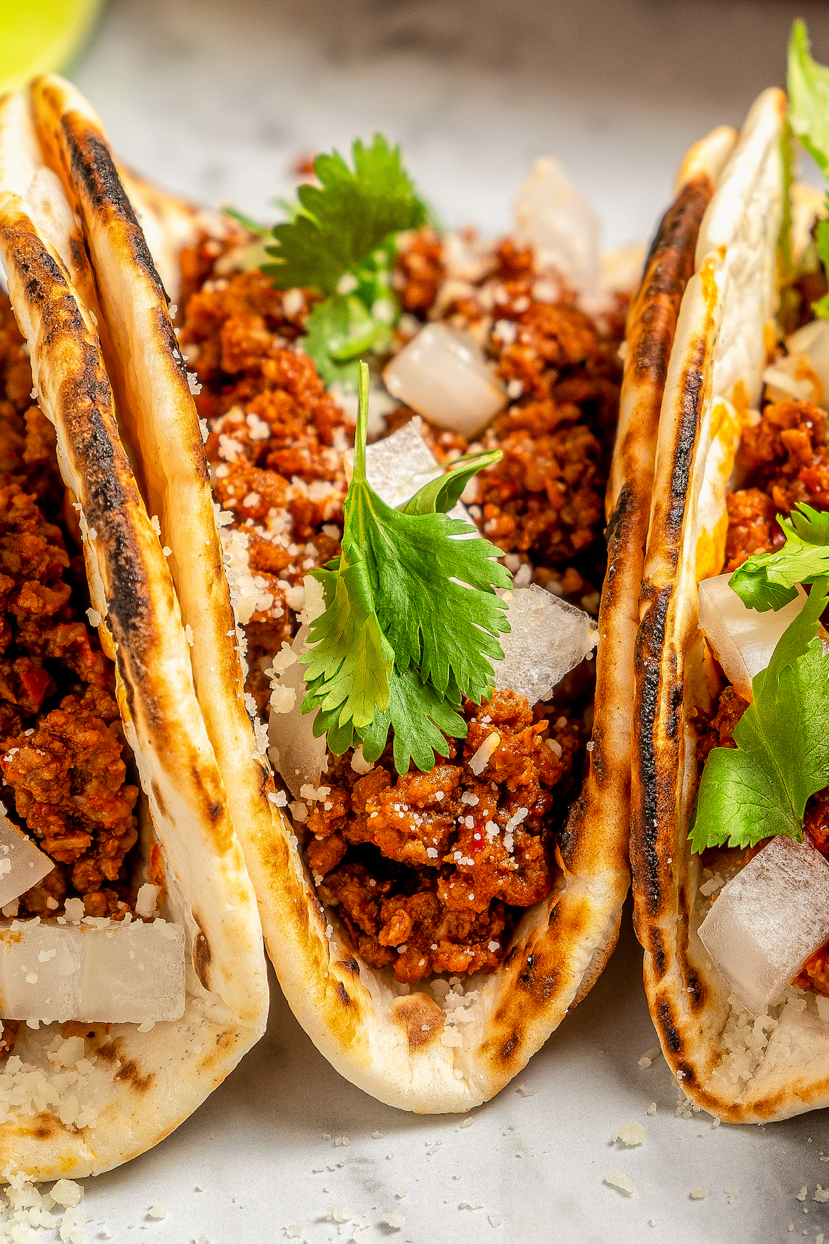 Spicy taco meat wrapped in tortillas with onion, cilantro and crumbled cheese on top.