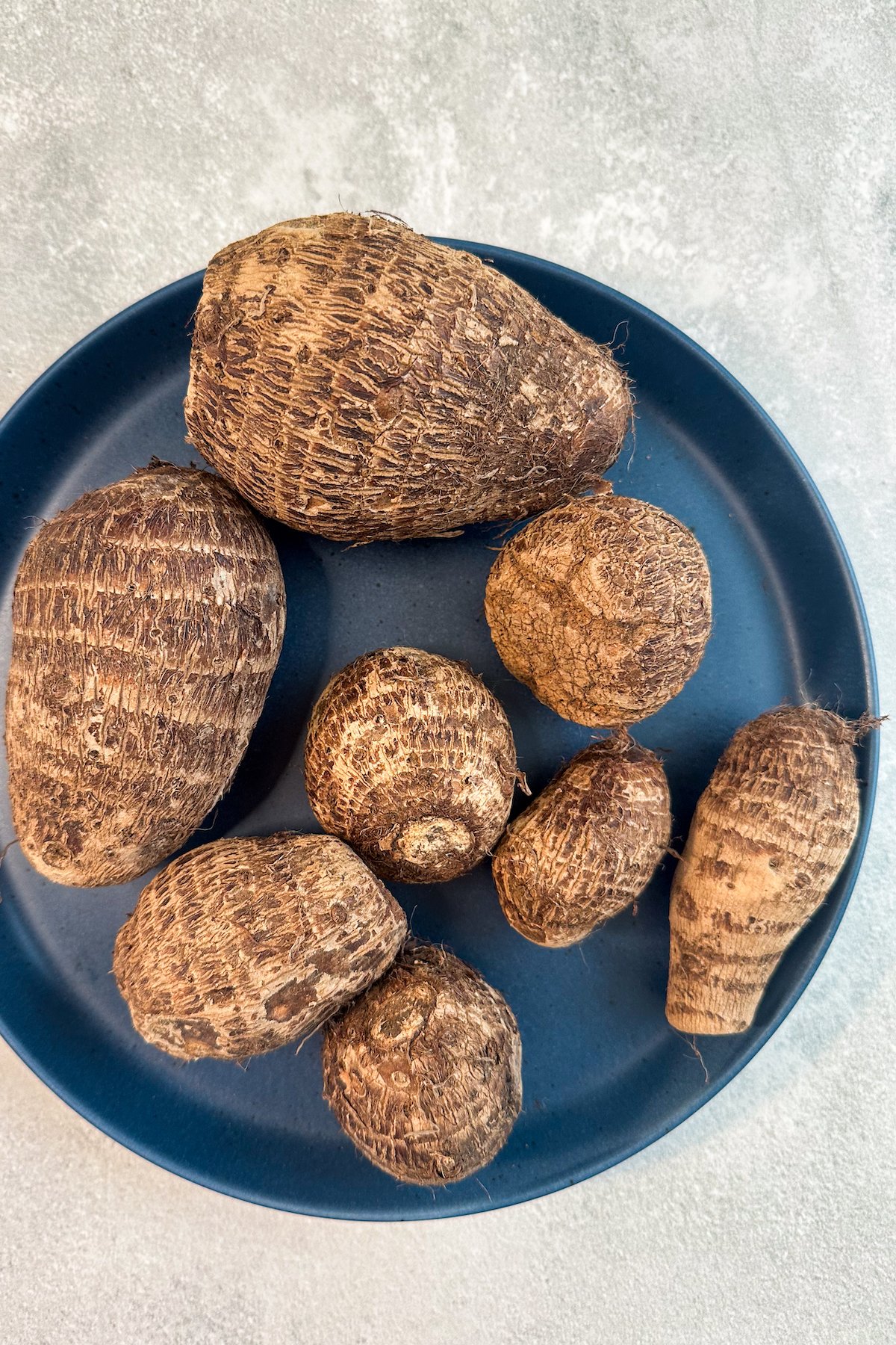 Whole taro roots on a blue plate.