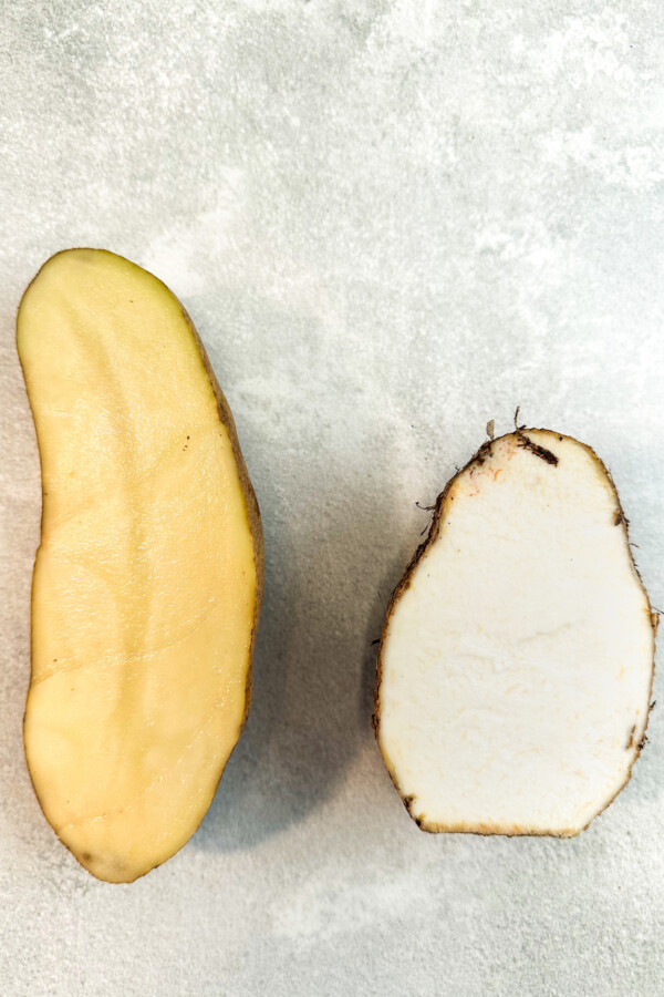 A potato sliced in half next to a taro root sliced in half.